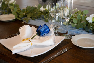 Decorations for the wedding receptions party have a single blue rose on each table setting for the guests