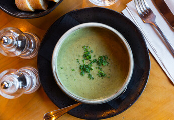 In clay pot there is thick cream soup-puree of vegetables, sprinkled with chopped herbs. Table is...