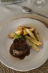 Gourmet gastronomy. Wedding main course. Top view of grilled loin tournedo with a red wine sauce and potatoes in a white dish on the table