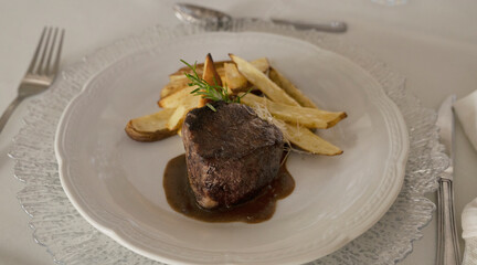 Gourmet gastronomy. Wedding main course. Closeup view of grilled loin tournedo with a red wine sauce and potatoes on the table with a beautiful glassware and tableware arrangement
