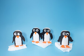Penguin crafts using painted cardboard tubes with googly eyes, orange beaks, and feet on faux ice. Creative kids project on light blue surface for school activities, holiday decor, DIY inspiration
