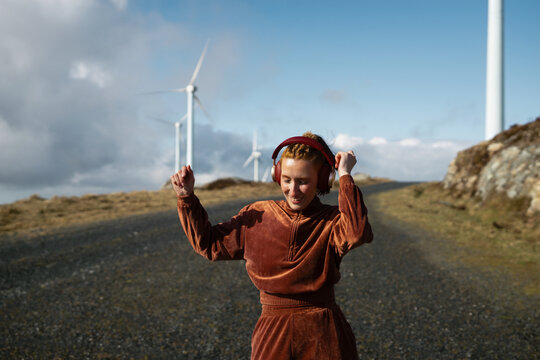 Young sporty woman dancing and listening to music in a wind farm