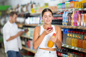 Girl in supermarket scan QR code bottle of soda. Female buyer photo information on packaging of bio...