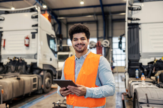 Portrait of happy diverse freight company coordinator with tablet in hands smiling at camera.