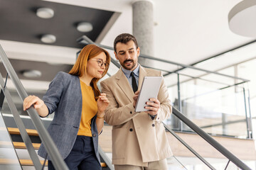 Businesspeople descending stairs at corporate office and looking at the tablet.