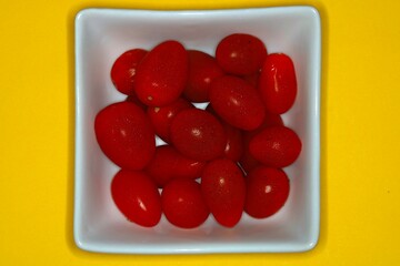 Fresh cherry tomatoes in a white bowl on a yellow background