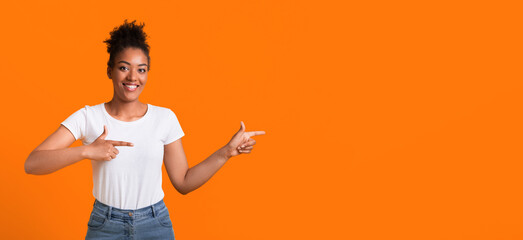 Look There. Smiling black girl pointing her fingers at copyspace over orange yellow studio wall, banner, panorama