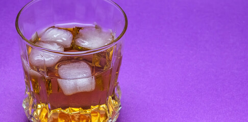 Detail of iced whiskey with purple background. The rich amber tones of the whiskey contrast elegantly. Selecive focus.