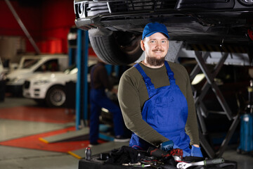 Young guy mechanic in uniform posing in car service station