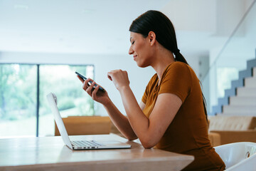 A woman sitting in the living room using a laptop and a smartphone look at camtalk by video call...