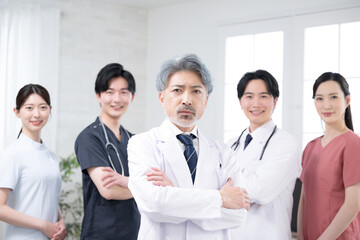カッコイイグレイヘアの医者と複数のドクターのイメージ　真剣な真面目な腕組のカメラ目線