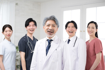 カッコイイグレイヘアの医者と複数のドクターのイメージ　笑顔のカメラ目線　大笑いで成功などのイメージ
