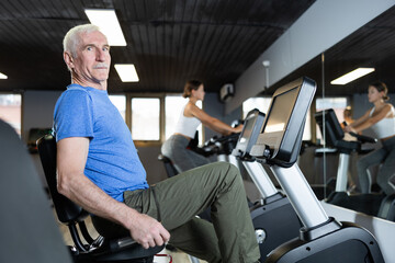 Elderly athletic man in sportswear training on exercise bike in gym
