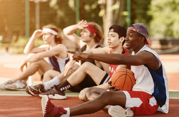 Fototapeta premium Millennial sportsmen communicating during their rest at basketball court, outdoos. Copy space