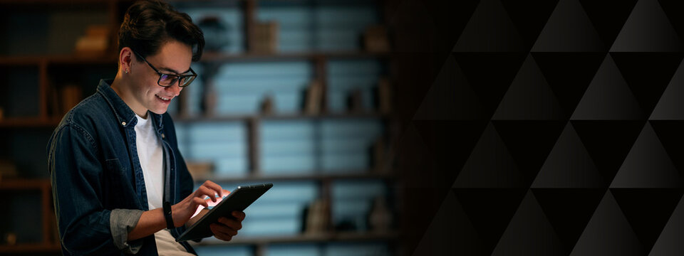 Smiling young businessman professional hold using digital tablet computer, using online app software on tech device modern pad, browse internet, communicate online, dark empty office, copy space - Powered by Adobe