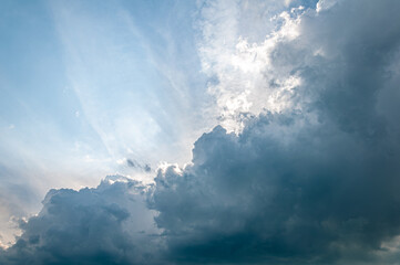 Obraz premium Moody sky with sun rays piercing through thick, dark storm clouds. A powerful atmospheric scene capturing the calm before a summer thunderstorm. Perfect for backgrounds or weather themes.