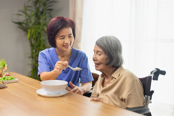 Caregiver feeding elderly asian woman with soup.