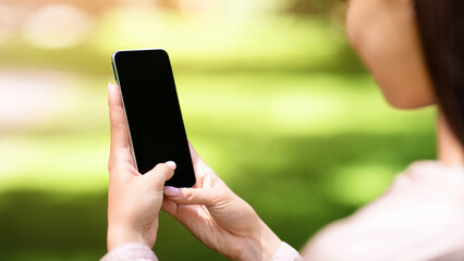 Woman using smartphone with blank black screen outdoors, mockup, over shoulder view with copy space for advertisement