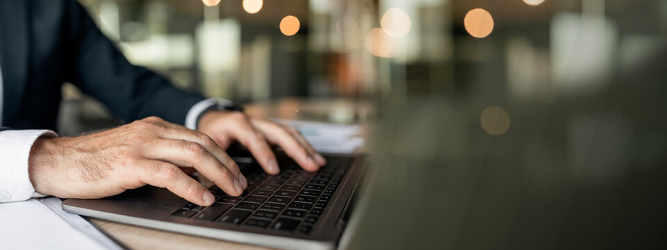 Closeup businessman using laptop, typing on keyboard, writing email, sitting at desk in office, selective focus. Accountant writing financial report, searching information