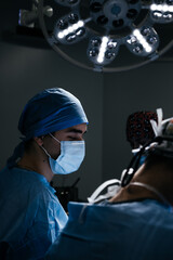 Portrait of a Male Doctor in mask in a Dark Hospital Room with Technological Equipment. Asian...
