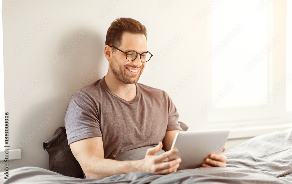 Aufkleber Happy Man Using Tablet Computer Browsing Internet Sitting In Bed At Home. Modern Lifestyle And Gadgets Concept