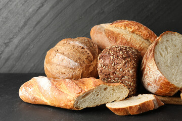 Whole and cut loafs of bread on black table, closeup
