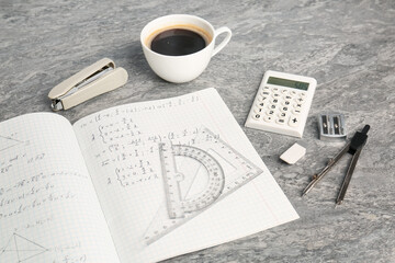 Doing homework. Notebook with math assignment, coffee and stationery on grey desk, closeup