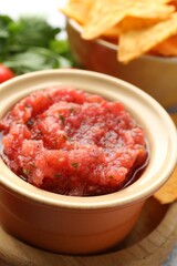 Spicy salsa sauce in bowl and nachos on table, closeup