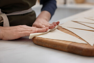 Woman rolling croissant from fresh dough at light table indoors, closeup