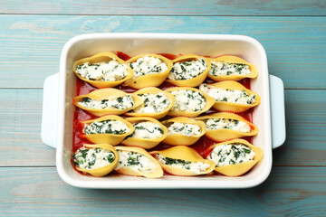 Delicious pasta with ricotta cheese, spinach and tomato sauce in baking dish on light blue wooden table, above view