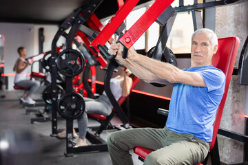 Elderly athletic man training her arms using machine in gym