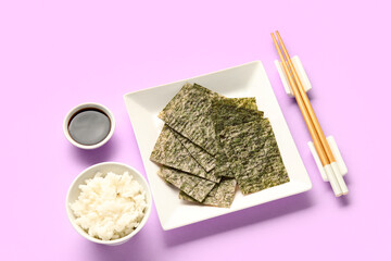 Plate with nori sheets, chopsticks, rice and soy sauce on color background