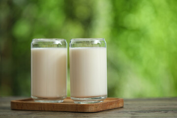 Board with glasses of fresh milk on wooden table outdoors