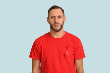 Obraz premium Young man with red ribbon on blue background. AID awareness concept