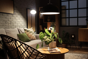 Interior of modern living room with grey sofa, wooden coffee table and glowing lamps at evening