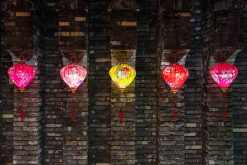 A collection of colorful lanterns beautifully hanging against a charming brick wall