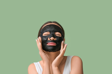 Young woman applying activated charcoal mask on her face against green background