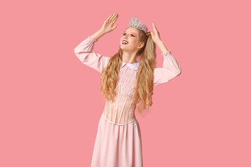 Beautiful young happy woman dressed as doll with crown on pink background