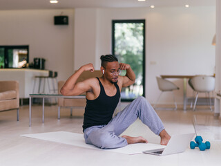 Training At Home. Sporty man doing the training while watching an online tutorial on a laptop,...