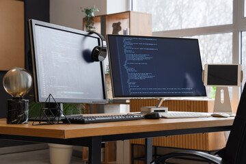 Computer monitors with programming code and headphones on desk in office