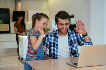 Obraz premium Work from home. Daughter interrupting her father while he is having a business online conversation on his laptop while sitting in the modern living room.