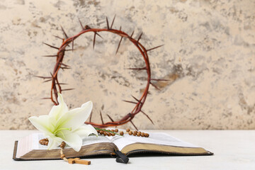Lily, prayer beads, Holy Bible and crown of thorns on white table near light wall
