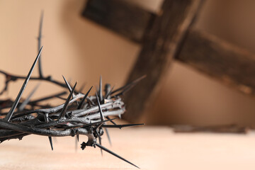 Crown of thorns with wooden cross on beige background, closeup. Good Friday concept