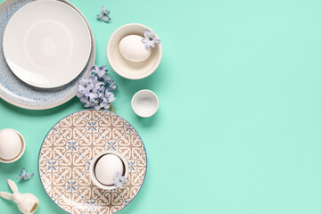 Stylish table setting with Easter eggs, flowers and toy bunny on turquoise background