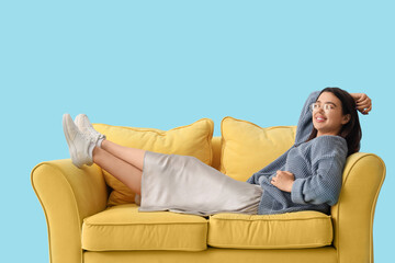 Fototapeta premium Young woman lying on yellow sofa against blue background