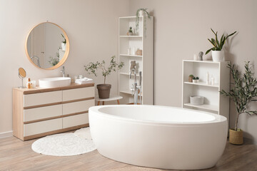 Bathtub, shelving unit, wooden chest of drawers with sink and bath supplies in interior of bathroom