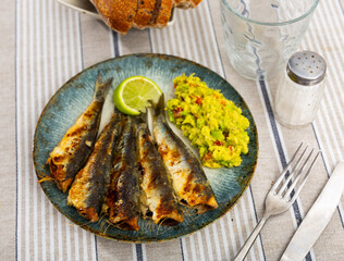 Carcasses of small Atlantic sardine fish, fried until golden brown. Fish dish is served with portion of mashed guacamole, slice of lime and rye bread.