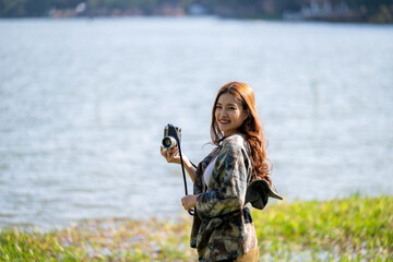 Naklejka premium A woman is standing on a grassy field near a body of water, holding a camera