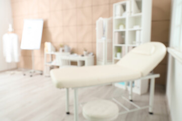 Blurred view of medical office with couch, doctor's workplace and shelf units