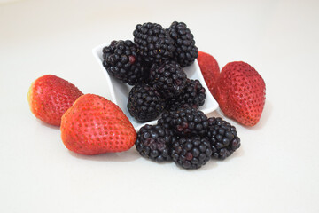 Blackberries spilling out of a white cup accompanied by vibrant strawberries